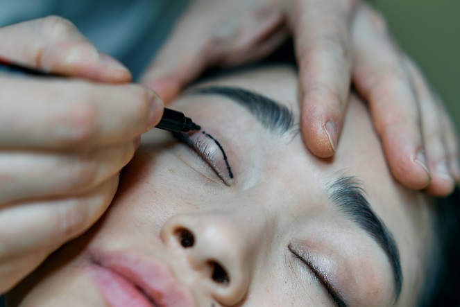 A person drawing a line on a young woman's eyelid