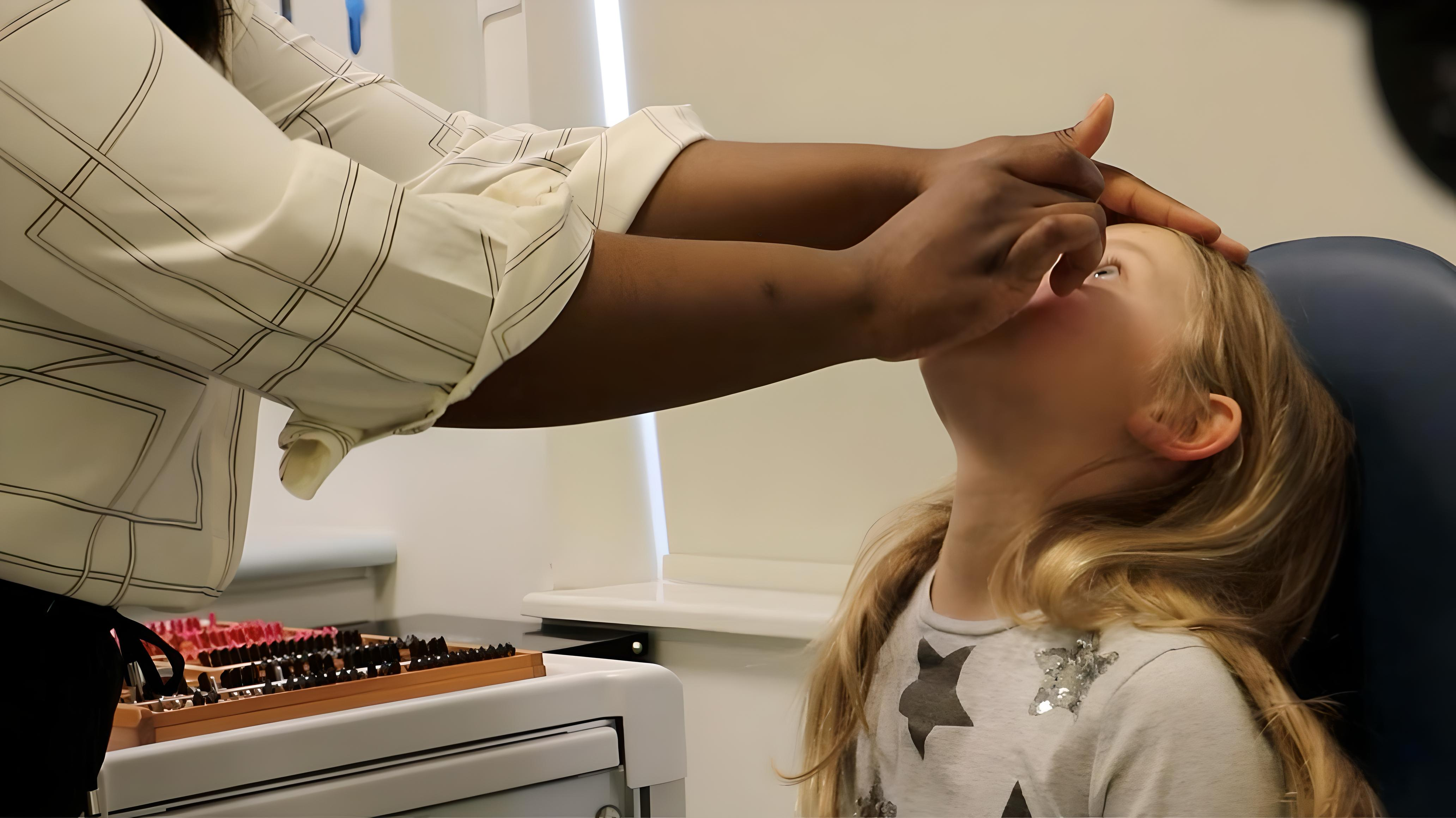 Child looking up as practitioner prepares to administer eye drops