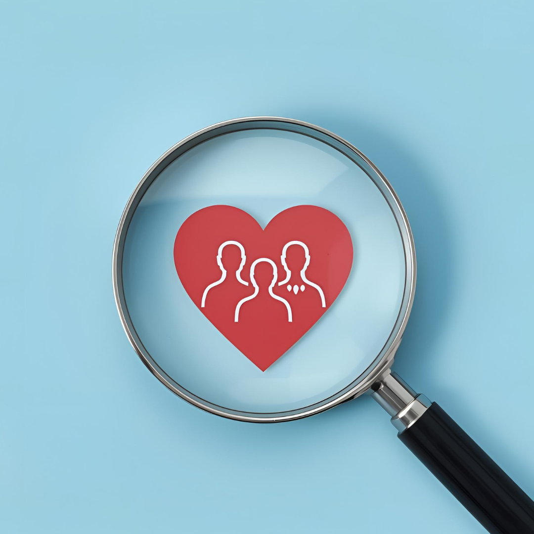 Red paper heart with the outline of three people underneath a magnifying glass on a blue background
