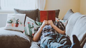 A person laying on a couch reading a book