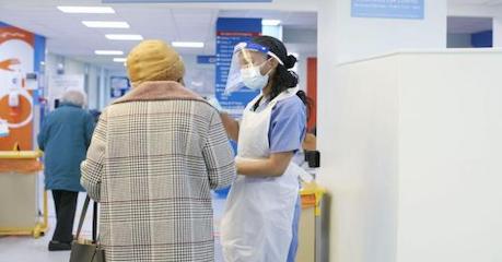 Masked nurse speaking with a patient in a hospital corridor
