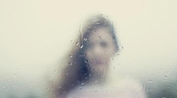 A photo of a young woman through a rainy window