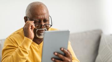 A mature man holding his glasses and looking at his laptop