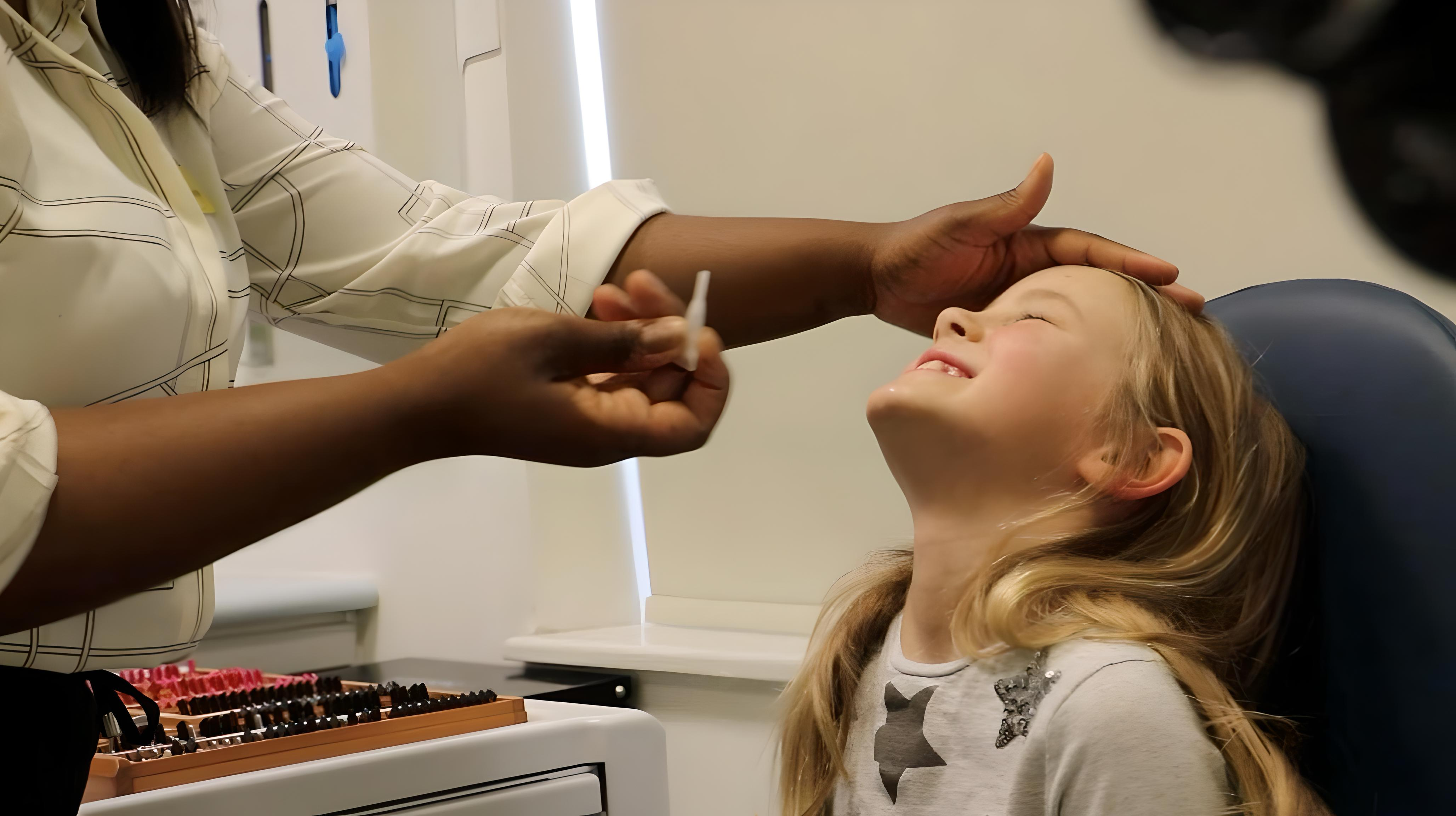 Child looking up as practitioner prepares to administer eye drops