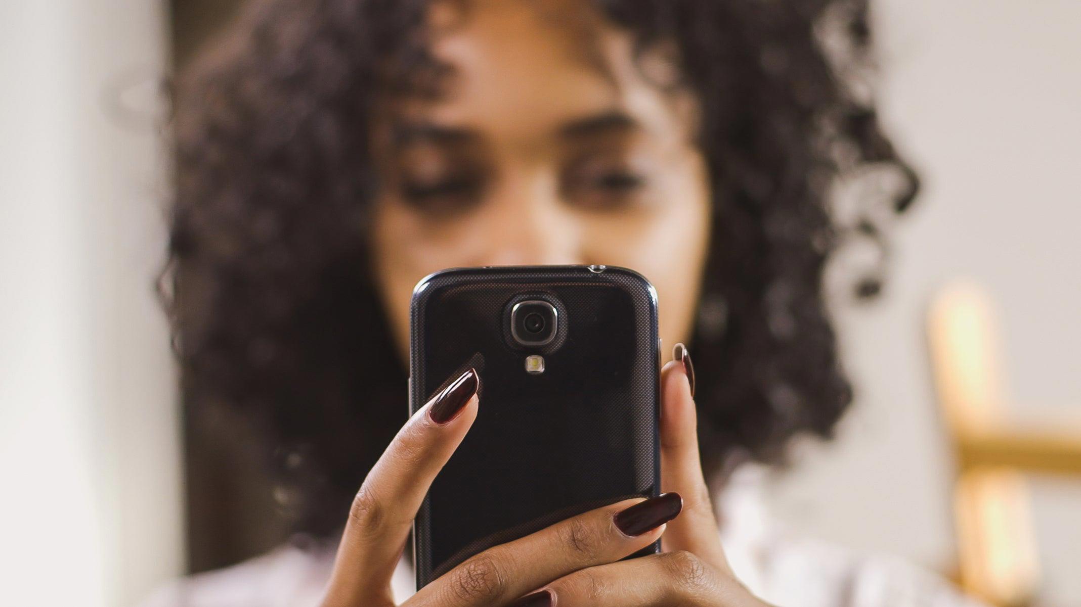 Blurred image of a person holding their mobile phone, the mobile phone is in focus in the foreground