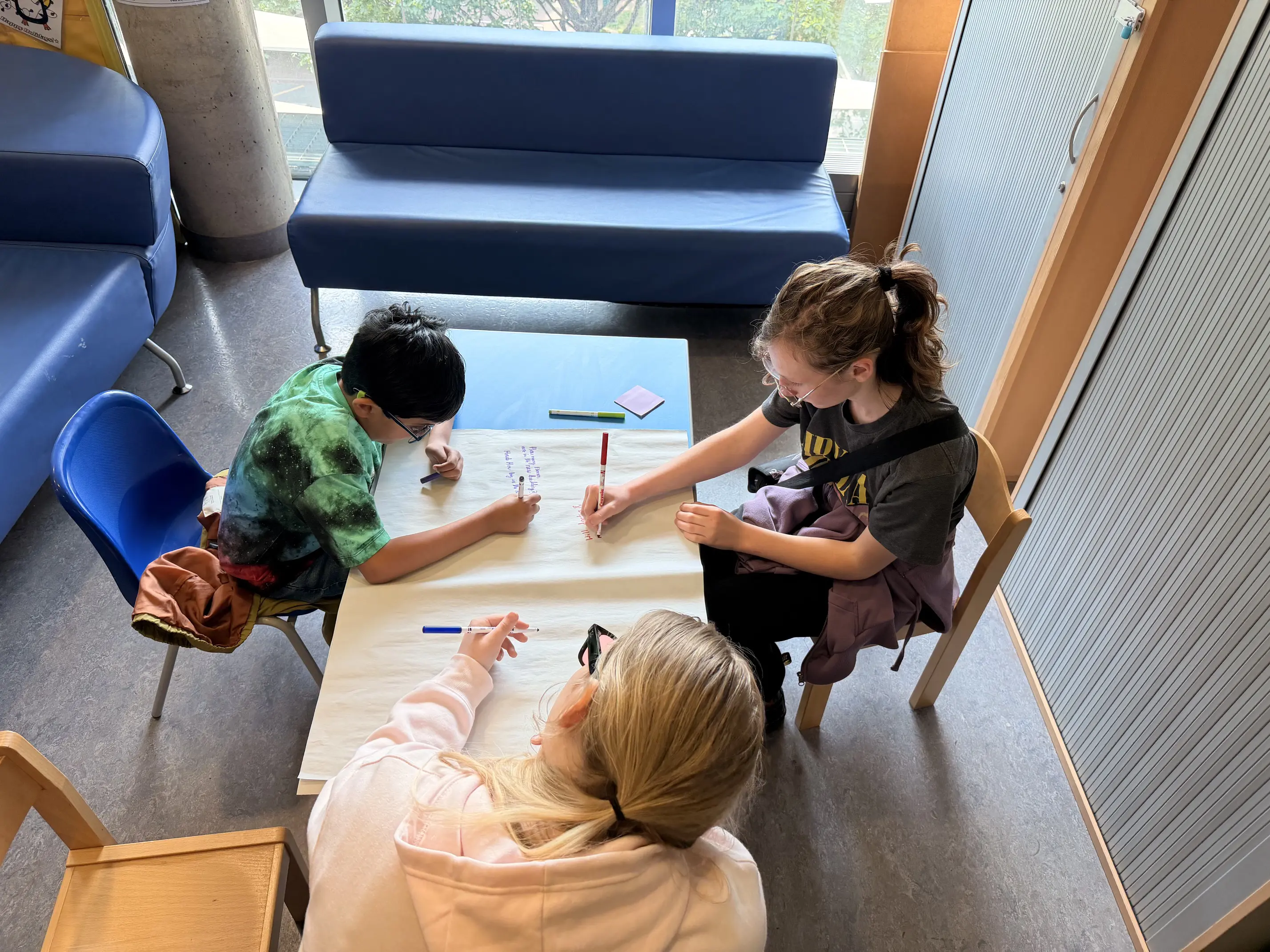 Three people of different ages siting around the table drawing on paper