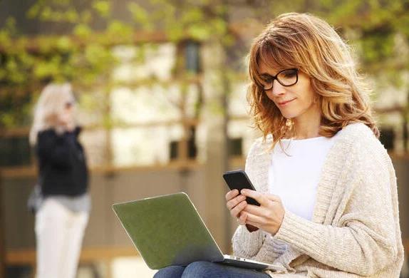 A woman sitting outside with her laptop and phone