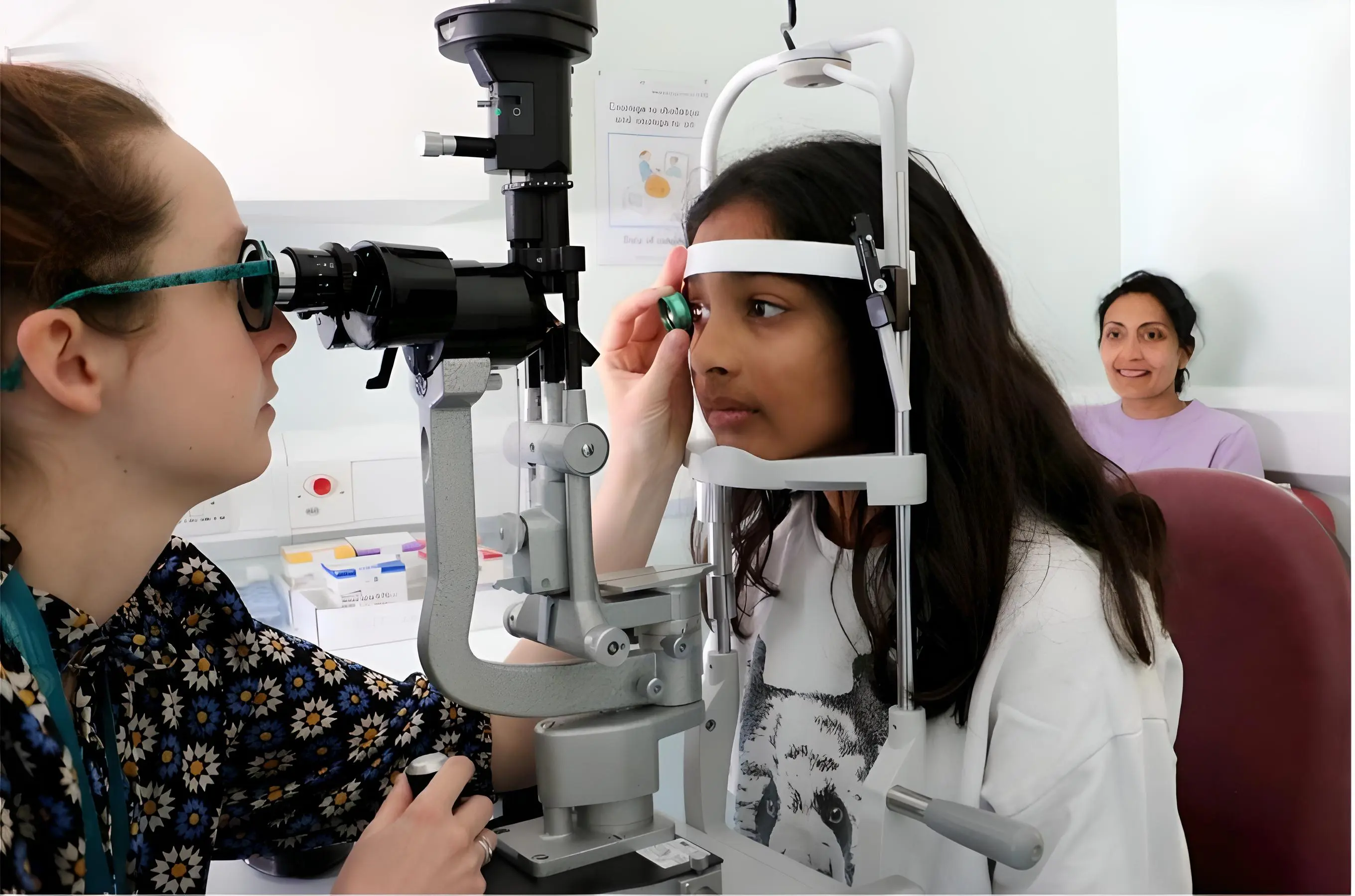 Consultant conducting an eye test on a young person in a hospital consultation room, their grown up is observing in the background